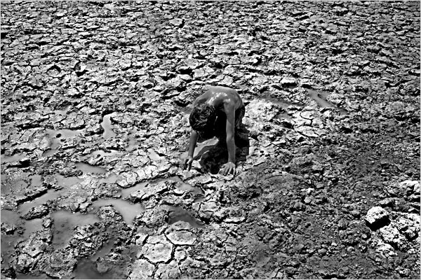 NYT caption: "A boy rested on the mud in a dried-up section of the Euphrates River near Jubaish, Iraq, in June."